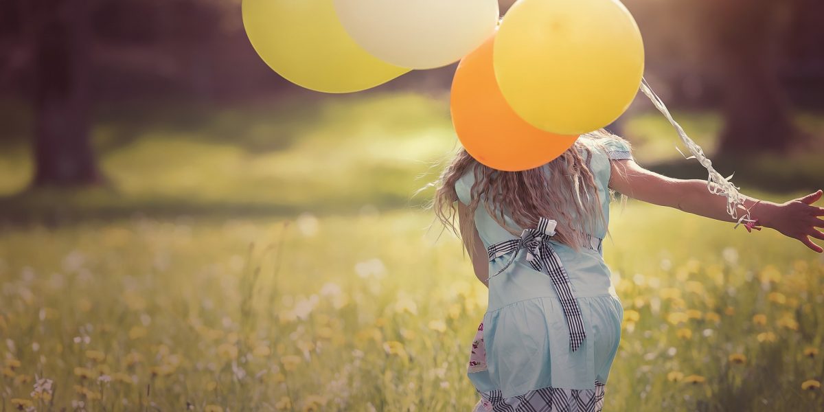 girl with long hair running through field with colourful balloons