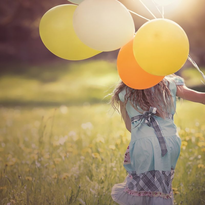 girl with long hair running through field with colourful balloons