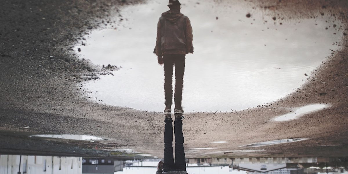 man looking at reflection in large puddle