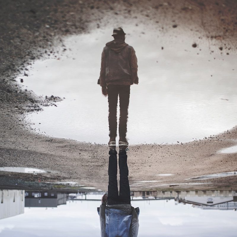 man looking at reflection in large puddle